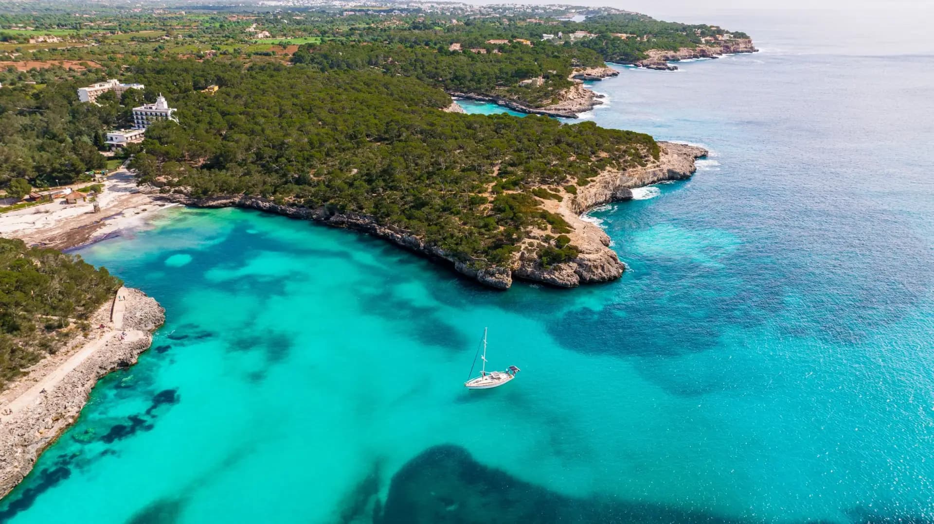 Ein Segelboot in einer türkisfarbenen Bucht an Mallorcas Küste